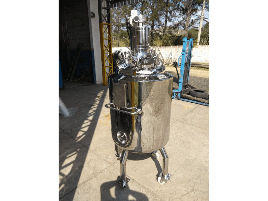 Reator químico industrial em aço inox com pés e rodízios, instalado em área de fábrica, utilizado em processos de mistura e reação química
